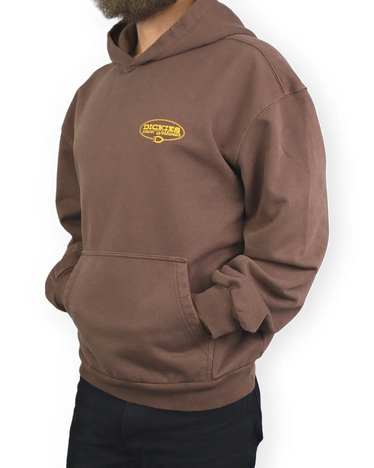 Dickies Avondale hoodie i brunt, snett från sidan med händerna i fickan, på modell