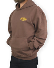 Dickies Avondale hoodie i brunt, snett från sidan med händerna i fickan, på modell